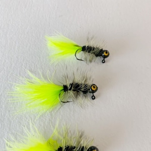 May include: Three black and yellow fishing lures with a feather tail. The lures have a black body with a yellow eye and a yellow feather tail.
