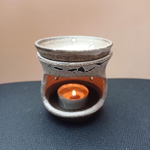 Może przedstawiać: Biały ceramiczny palnik do olejków eterycznych z małą świeczką typu tealight w środku. Palnik ma fakturowaną powierzchnię i mały otwór na świeczkę.