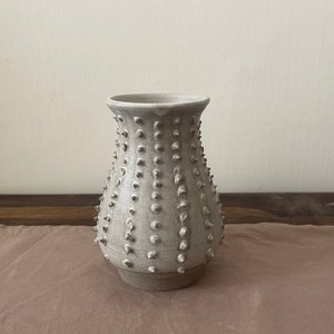 May include: A white ceramic vase with a textured, spiky surface. The vase has a rounded base and a narrow opening.