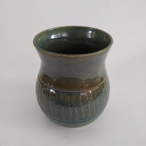 May include: A green and brown ceramic vase with a ribbed design. The vase has a wide mouth and a rounded bottom.
