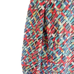 May include: A colorful long-sleeve blouse with a geometric pattern. The pattern features red, blue, yellow, and gray zigzags on a white background. The blouse has a high neckline and gathered sleeves.