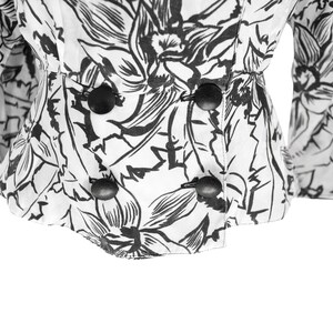 Puede incluir: Una blusa blanca con estampado floral negro y cuatro botones negros en la parte delantera.
