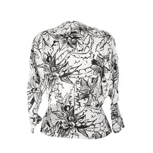 Puede incluir: Una blusa blanca con estampado floral negro. El estampado presenta flores y hojas grandes y estilizadas.