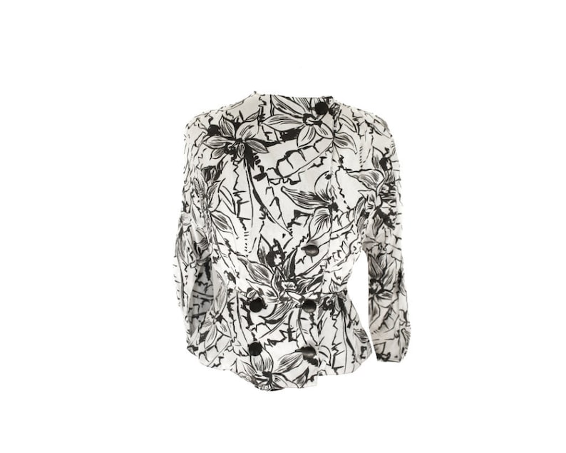Puede incluir: Una blusa blanca con estampado floral negro. La blusa tiene un corpi&ntilde;o ajustado y mangas largas.