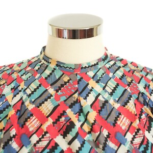 May include: A colorful patterned shirt with a high collar. The shirt features a geometric design with red, blue, black, gray, and yellow accents. The shirt is displayed on a mannequin.