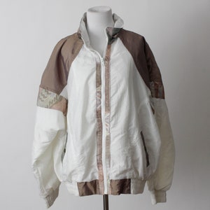 May include: A white windbreaker jacket with brown and beige patterned sleeves. The jacket has a zipper closure and a stand-up collar.