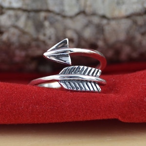May include: A silver ring with a twisted arrow design. The arrow has a feathered tail and a pointed tip.