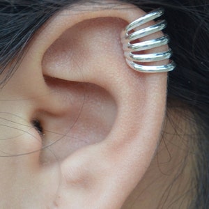 May include: Silver ear cuff with multiple rings, designed to be worn on the upper cartilage of the ear.