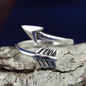 May include: A silver ring with a twisted arrow design. The arrow is pointing upwards and the ring is open on one side.