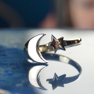 May include: A silver ring with a crescent moon and a star design. The ring is adjustable and can be worn on any finger.