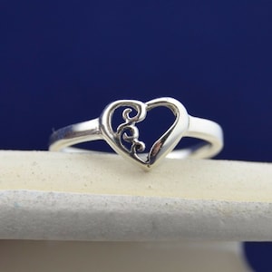May include: A silver ring with a delicate heart-shaped design. The heart is open and features a swirling, intricate pattern.