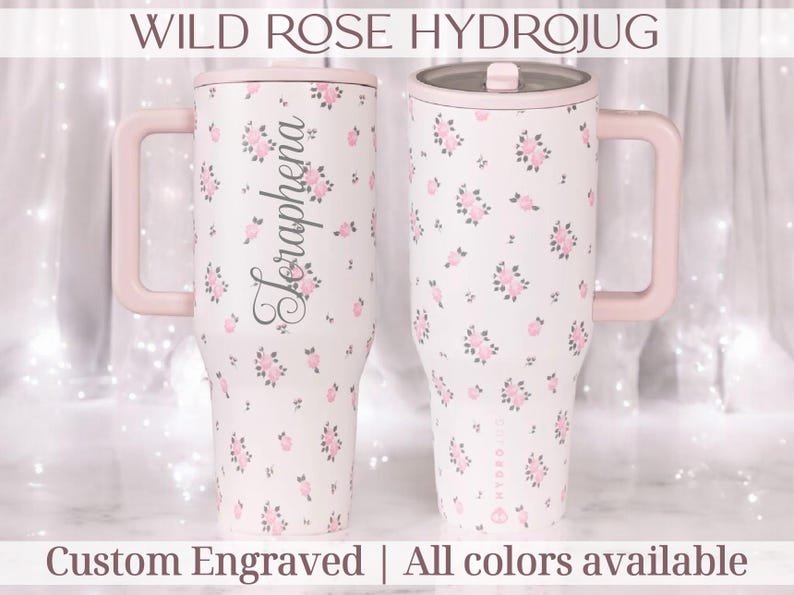 May include: Two white Hydrojugs with pink handles and lids, adorned with pink floral patterns. One jug features the name "Seraphena" in script. The text "WILD ROSE HYDROJUG" and "Custom Engraved | All colors available" are displayed.