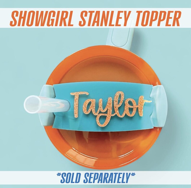 May include: An orange and teal Stanley topper with a straw. The topper has the name "Taylor" in gold glitter lettering. The text "SHOWGIRL STANLEY TOPPER" is at the top. The text "*SOLD SEPARATELY*" is at the bottom.