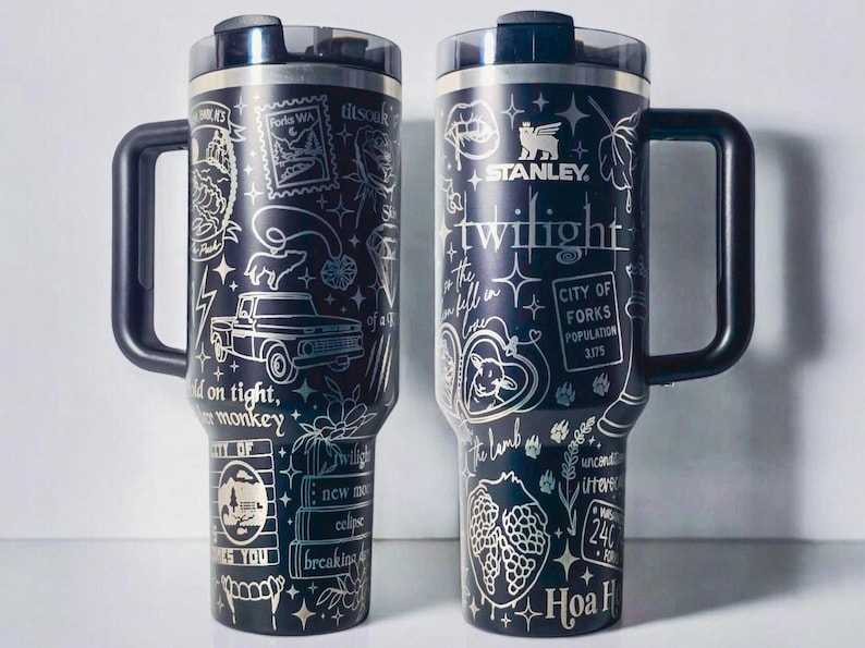 May include: Two black Stanley tumblers with silver etched designs. One features a truck, bear, and text "Hold on tight, you monkey." The other has "Twilight" and "City of Forks" text. Both have handles.