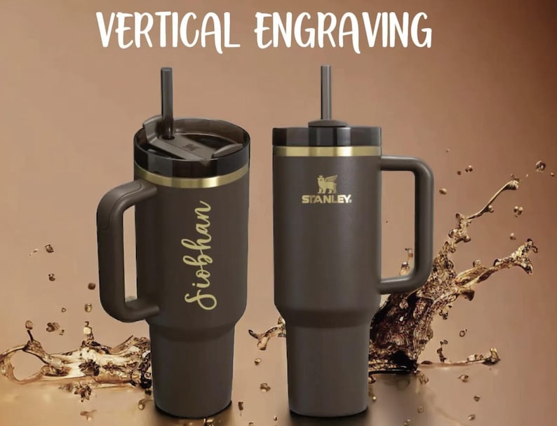 Puede incluir: Dos vasos Stanley marrones con asas y pajitas. Uno est&aacute; grabado con un nombre en escritura dorada. El otro presenta el logotipo de Stanley. El texto "VERTICAL ENGRAVING" est&aacute; en la parte superior.