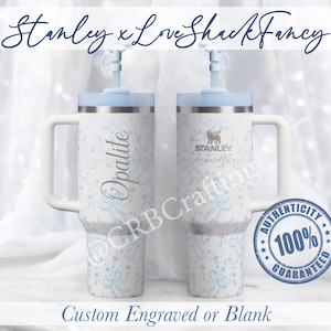 May include: Two white and stainless steel Stanley tumblers with light blue lids and handles. The tumblers feature a floral pattern and the word "Opalite". The text "Stanley x Love Shack Fancy" is at the top.