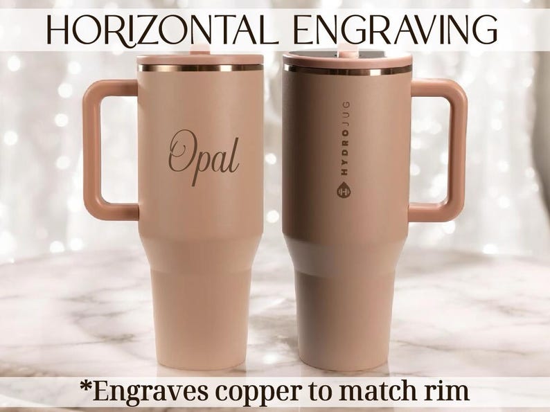 May include: Two insulated travel mugs in a light peach colour with copper-coloured rims and handles. One mug has the name "Opal" engraved on it. The other mug has the text "HYDROJUG" printed vertically. The text "*Engraves copper to match rim" is at the bottom.