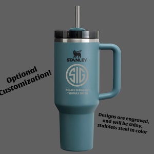 Puede incluir: Una taza de viaje de acero inoxidable azul con una tapa negra y una pajita. La taza tiene un asa y est&aacute; grabada con el logotipo de Stanley, las letras "SIG", "Police Sergeant" y "Thomas Smith".