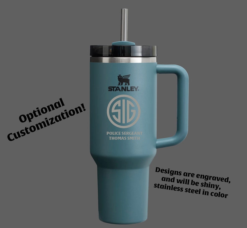Puede incluir: Una taza de viaje de acero inoxidable azul con una tapa negra y una pajita. La taza tiene un asa y est&aacute; grabada con el logotipo de Stanley, las letras "SIG", "Police Sergeant" y "Thomas Smith".