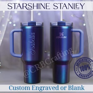 May include: Two blue Stanley tumblers with handles and straws. One tumbler has the name "Isabella" engraved on it. The text "STARSHINE STANLEY" and "Custom Engraved or Blank" are also visible.