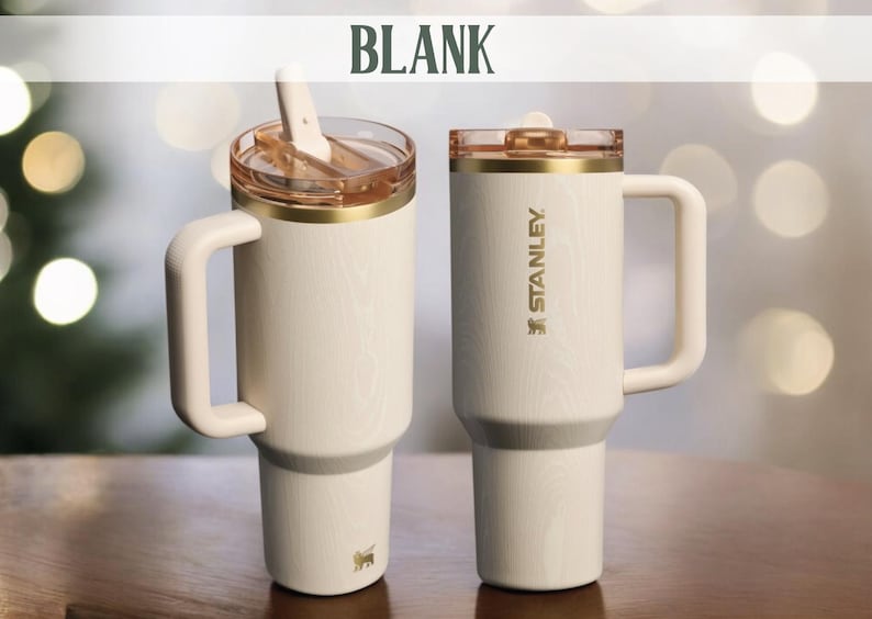 May include: Two cream-colored Stanley travel mugs with handles. One has a clear lid with a straw, the other has a clear lid. Both have gold accents and the Stanley logo. The word "BLANK" is at the top.