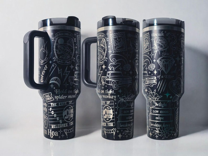 May include: Three black travel mugs with silver etched designs and handles. Each mug features unique illustrations, including text, lightning bolts, and a diamond. The mugs have a black lid and a handle. The text on the mugs includes "Hold on tight, spider monkey" and "Twilight, new moon, eclipse".