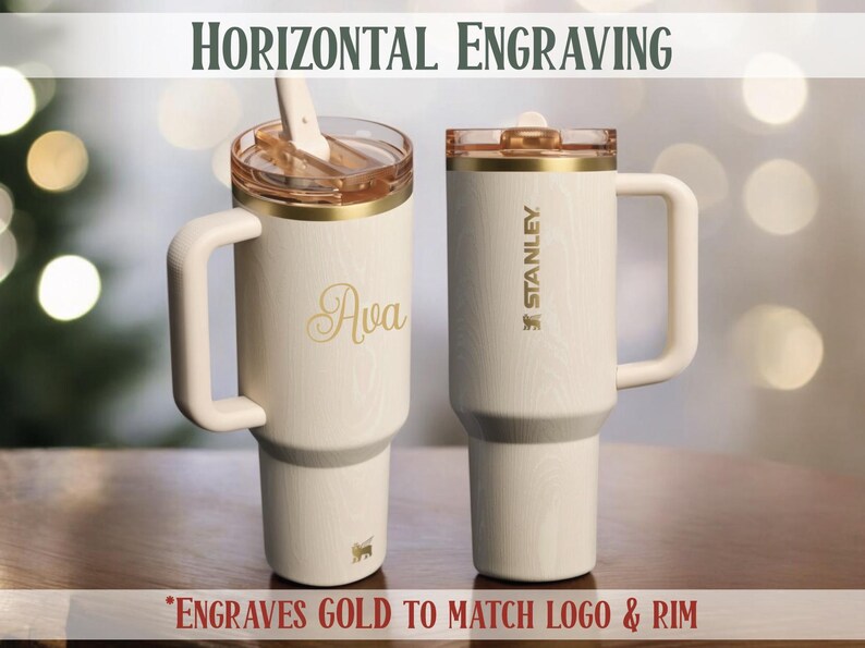 May include: Two cream-colored Stanley tumblers with gold accents and handles. One tumbler is engraved with the name "Ava" in gold script. The other features the Stanley logo. Both have gold rims and lids. The text "HORIZONTAL ENGRAVING" is at the top.