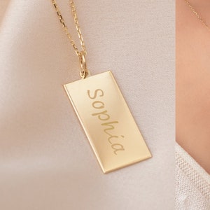 May include: A gold chain necklace with a rectangular pendant engraved with the name "Sophia".