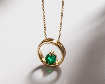 May include: A gold necklace with a circular pendant featuring a green emerald gemstone.