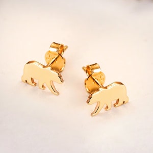Puede incluir: Pendientes de botón dorados con forma de oso. Los pendientes presentan una silueta detallada de oso. La imagen también muestra los estilos de cierre de rosca y de presión. Estos pendientes son un complemento encantador.