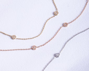 May include: Three delicate gold chain bracelets with small round charms set with tiny diamonds. The bracelets are layered on a white background.