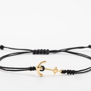 Könnte beinhalten: Ein verstellbares schwarzes Armband mit einem goldenen Anker-Anhänger. Das Armband wird mit verschiedenen farbigen Schnüren gezeigt, darunter Burgunderrot, Grün, Creme, Lila, Blau, Rot und Schwarz.