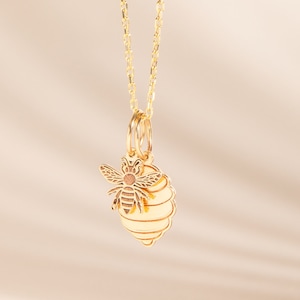 Könnte beinhalten: Eine goldene Kettenkette mit einem Anhänger, der eine Biene und ein Wabenmuster zeigt.