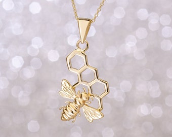 May include: Gold necklace with a bee and honeycomb pendant. The bee is detailed and has wings. The honeycomb is a geometric design.