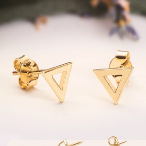 May include: A pair of gold triangle stud earrings with a screw back closure style. The earrings are simple and minimalist, making them a versatile accessory for any occasion.