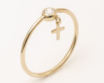 May include: Gold ring with a small diamond and a dangling cross charm. The ring is available in a variety of colors and charms, including a heart, star, lightning bolt, cross, lightning bolt, crescent moon, and feather.