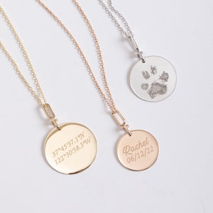 May include: Three gold necklaces with round pendants. The pendant on the left has the coordinates 37°45'37.1"N 122°30'38.3"W engraved on it. The pendant in the middle has the name "Rachel" and the date "06/12/22" engraved on it. The pendant on the right has a paw print engraved on it.