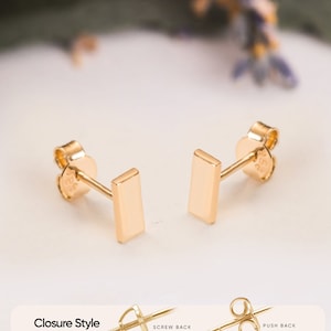 Puede incluir: Pendientes de barra de oro con cierre de rosca. Los pendientes se muestran sobre una superficie blanca.