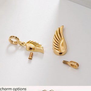K&ouml;nnte beinhalten: Ein goldfarbener Engelsfl&uuml;gel-Anh&auml;nger mit einer Schraub&ouml;ffnung. Der Anh&auml;nger ist zerlegt dargestellt mit einer kleinen Schraube und einer separaten Anh&auml;ngeroption. Die Anh&auml;ngeroptionen sind ein Kreuz und ein Schl&uuml;sselanh&auml;nger. Der Text "Your Engraving Personalization: 2 - Cross Charm 3 - Key Charm" wird unter den Anh&auml;ngern angezeigt.