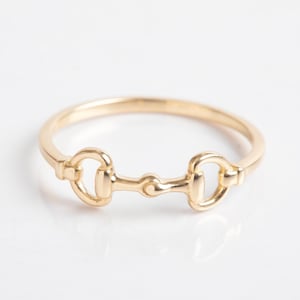 May include: A gold-toned ring with a double-loop design, resembling a horse's bit.