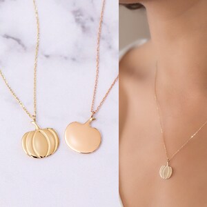 Puede incluir: Dos collares de oro con colgantes de calabaza. Un collar tiene un colgante de calabaza detallado, mientras que el otro tiene un colgante de calabaza liso y s&oacute;lido.