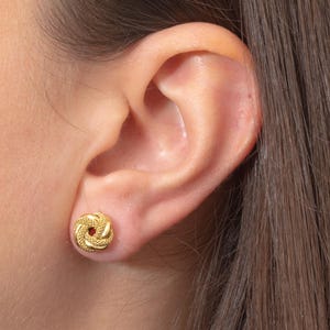 May include: Gold knot-shaped stud earrings. The earrings are small and delicate, and they are a classic and elegant style.