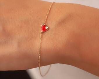 May include: A gold chain bracelet with a red enamel heart charm and a single diamond accent.