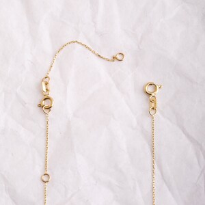 May include: A gold chain necklace with a lobster clasp and a jump ring. The chain is delicate and has a simple design.