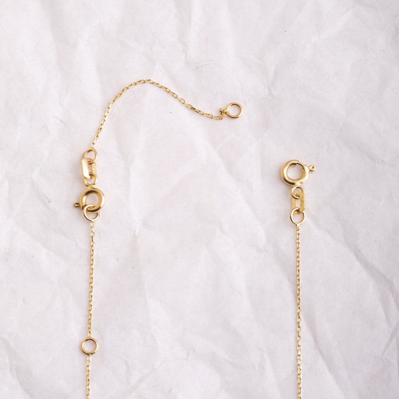 May include: A gold chain necklace with a lobster clasp and a jump ring. The chain is delicate and has a simple design.