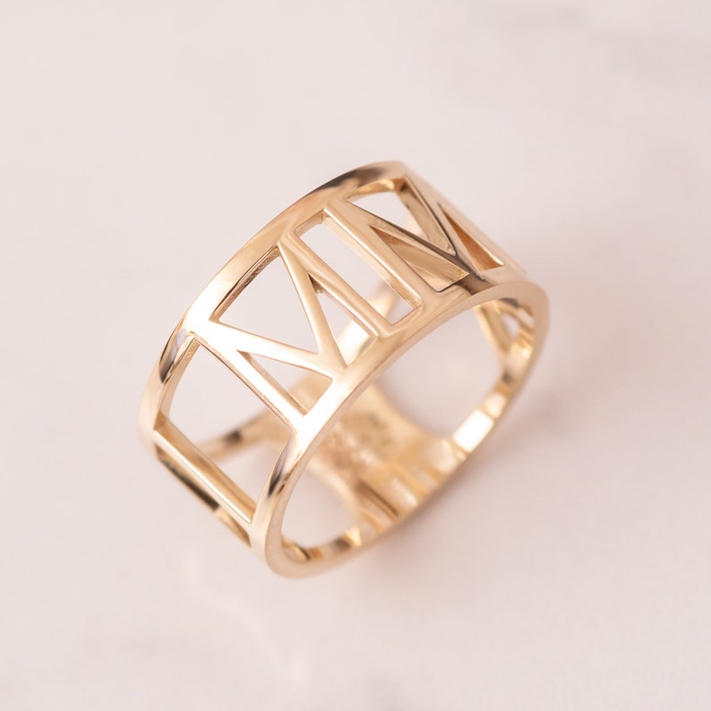 A stylish gold ring featuring a unique cut-out design with Roman numerals, perfect for adding a touch of elegance to any outfit. Crafted with precision, this handmade ring offers a luxurious feel and versatile design, suitable for daily wear or special occasions.