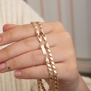 May include: Two gold chains, one with a slightly larger link than the other, are held in a hand. The chains are both made of a shiny, yellow gold.