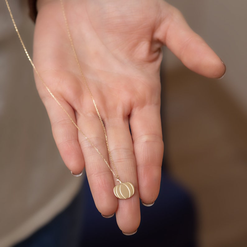 Puede incluir: Un collar de cadena de oro con un peque&ntilde;o colgante de calabaza detallado.