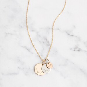 May include: A gold-colored necklace with three pendant charms. The largest charm is a gold disc with the engraved words "we loved". The other charms are a silver disc with "A&B" and a small rose gold charm with an infinity symbol.