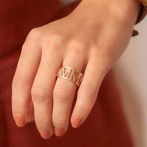 Pode incluir: Um anel dourado com um design de algarismos romanos. O anel &eacute; feito de metal e tem uma banda larga.